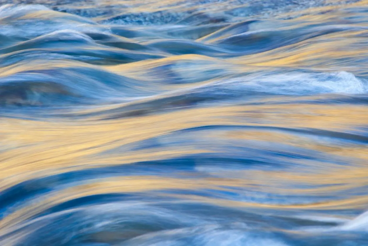 Close-up of water ripples reflecting blue and golden hues.