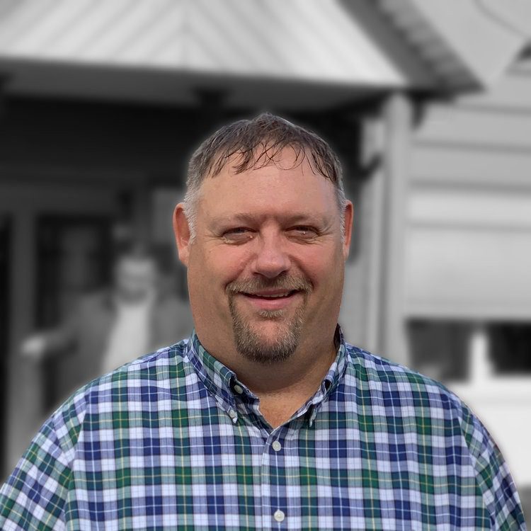 Man smiling outdoors in a plaid shirt.