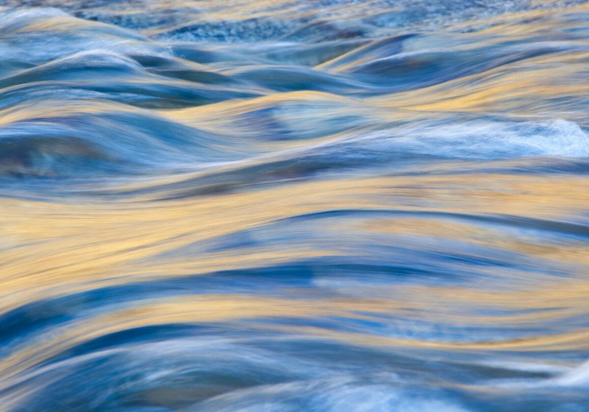 Close-up of water ripples reflecting blue and golden hues.